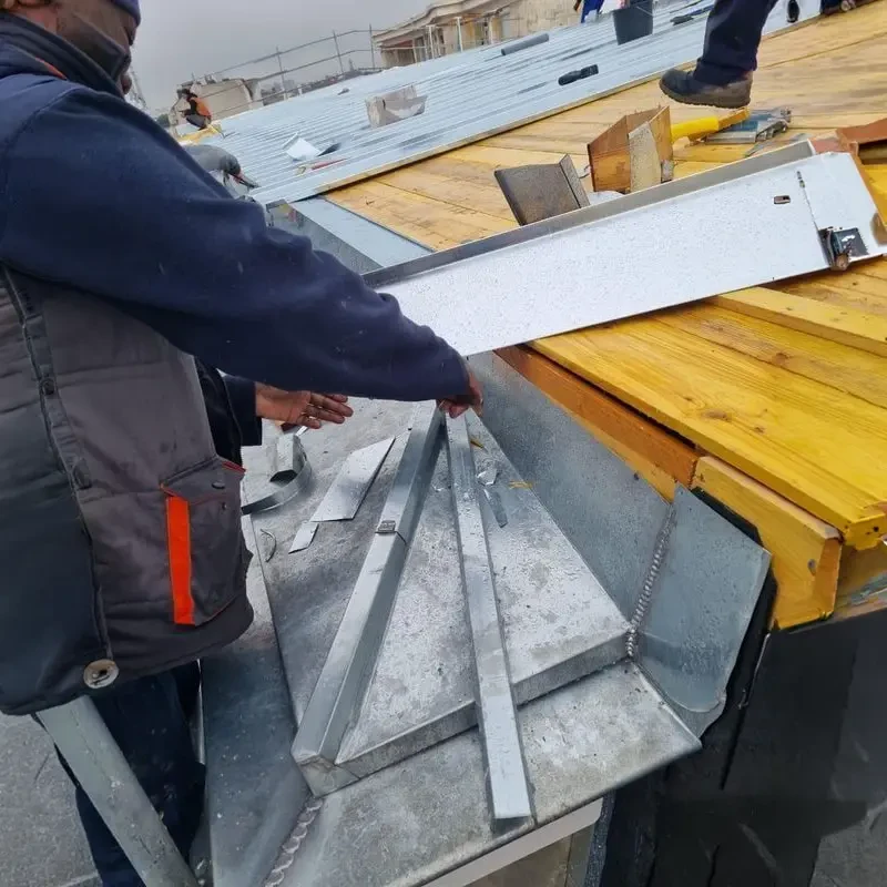 Ouvrier en combinaison de protection intégrale blanche travaillant sur toiture en ardoises, utilisant une échelle aluminium pour accéder aux tuiles défaillantes