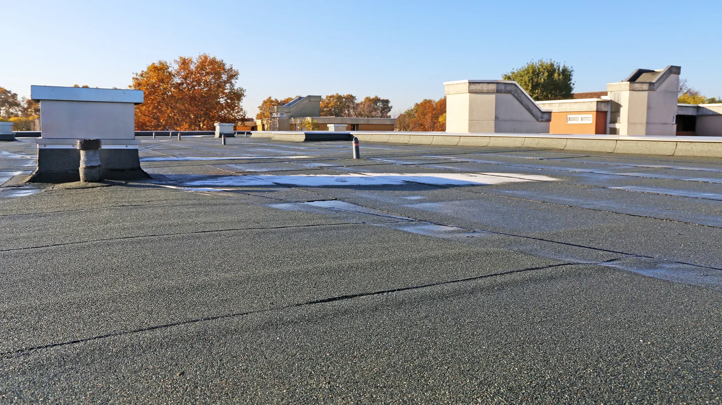Photographie d'un toit-terrasse plat en cours de r&eacute;novation, montrant la pose d'une membrane d'&eacute;tanch&eacute;it&eacute; par un professionnel en gilet de chantier. La vue devrait &ecirc;tre d'en haut ou de c&ocirc;t&eacute;, montrant clairement l'application des mat&eacute;riaux d'&eacute;tanch&eacute;it&eacute; sur la surface plane du toit, les joints, et les d&eacute;tails techniques du travail. L'image doit &ecirc;tre nette, professionnelle, de jour, et montrer concr&egrave;tement le type de travail r&eacute;alis&eacute; par l'entreprise en mati&egrave;re d'&eacute;tanch&eacute;it&eacute;.